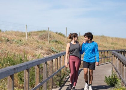 A couple in activewear strolling together on a sunny boardwalk in a natural setting.