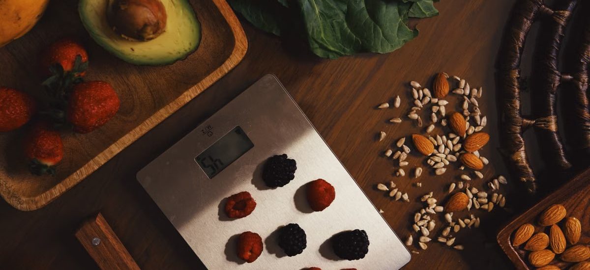 Top view of composed raw almond with seeds and avocado on table with berries on scales for cooking healthy dish